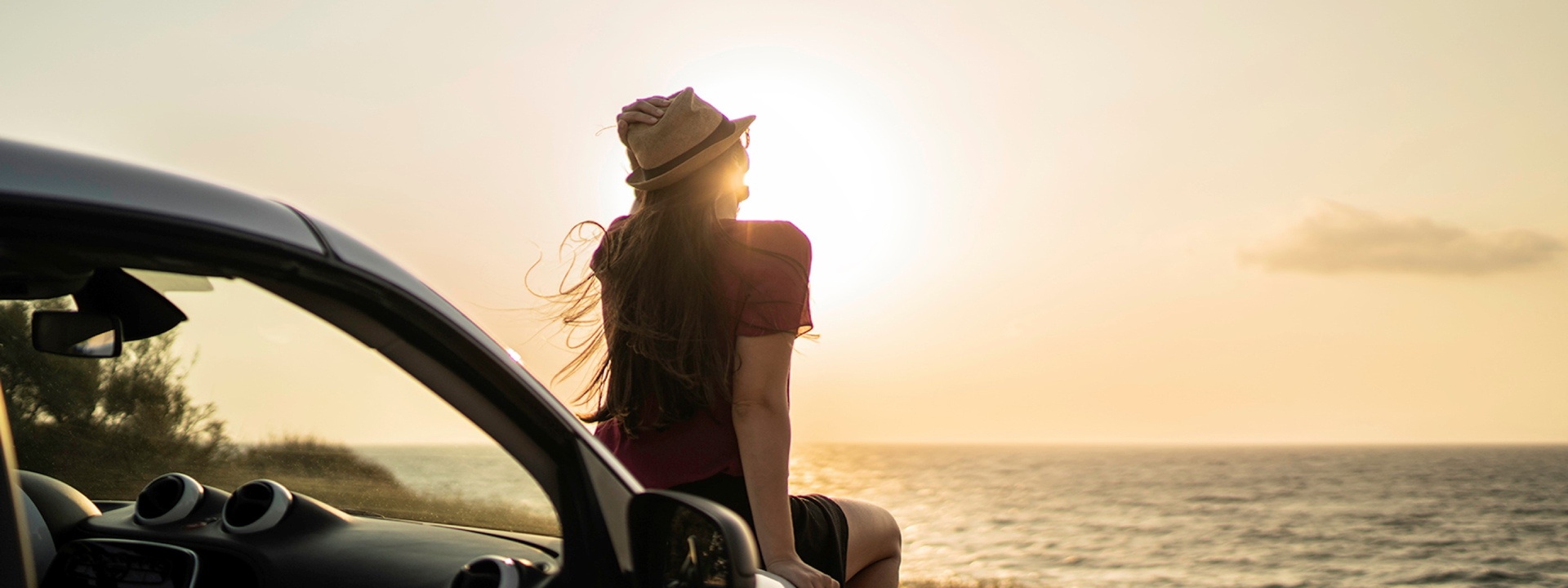 Sea sunset and a woman sitting on the car hood