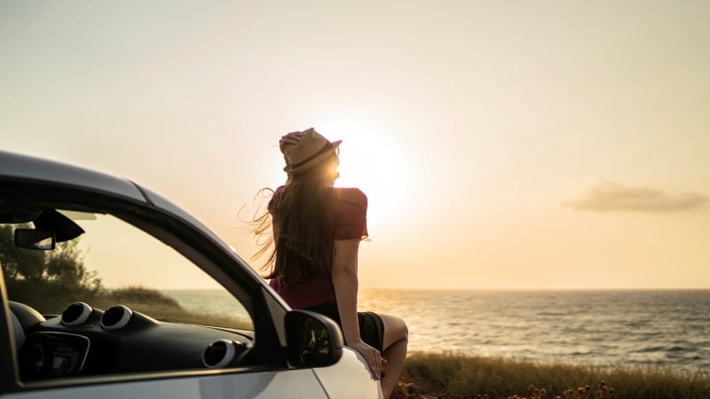 Sea sunset and a woman sitting on the car hood